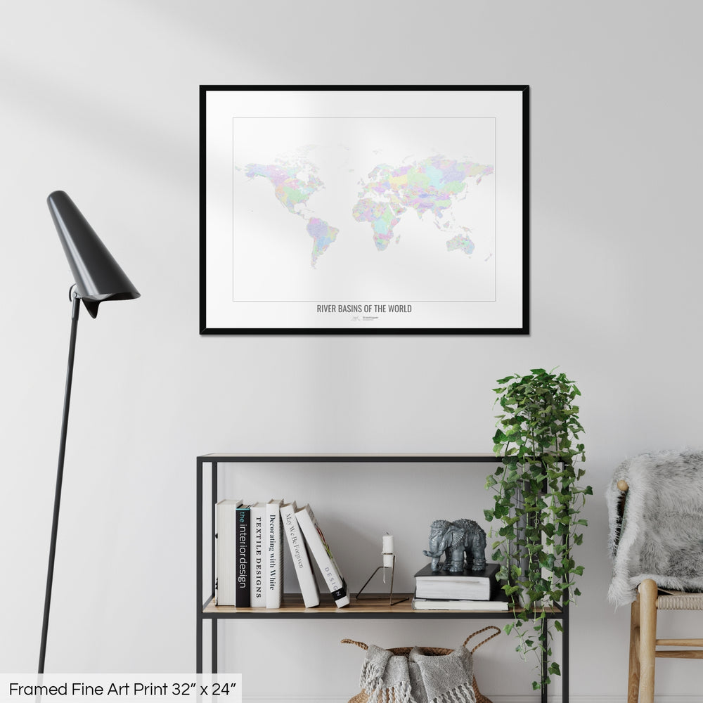 A colourful Grasshopper Geography map on a white wall, home decor in a living room. The map is in a black frame with a thick white mat. The title of the map is printed on the mat. The map hangs above a black shelf with plants and books on. A black lamp stands in the corner.