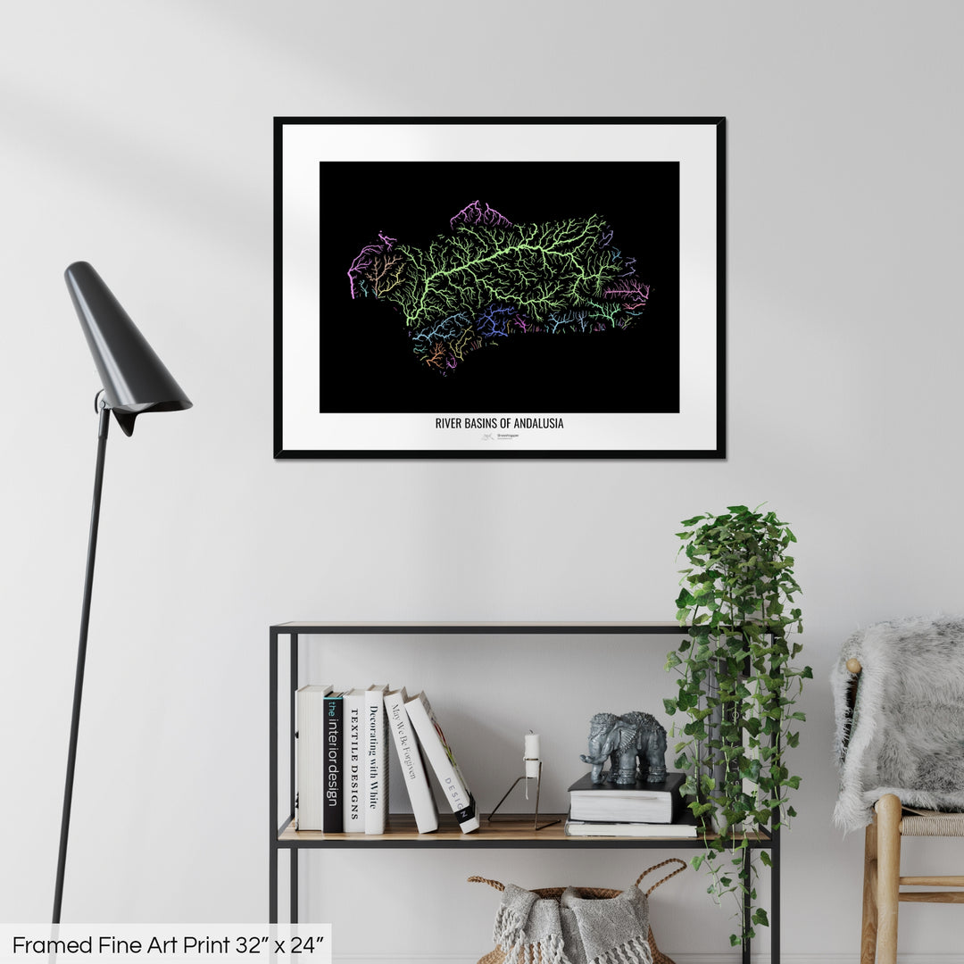 A colourful Grasshopper Geography map on a white wall, home decor in a living room. The map is in a black frame with a thick white mat. The title of the map is printed on the mat. The map hangs above a black shelf with plants and books on. A black lamp stands in the corner.