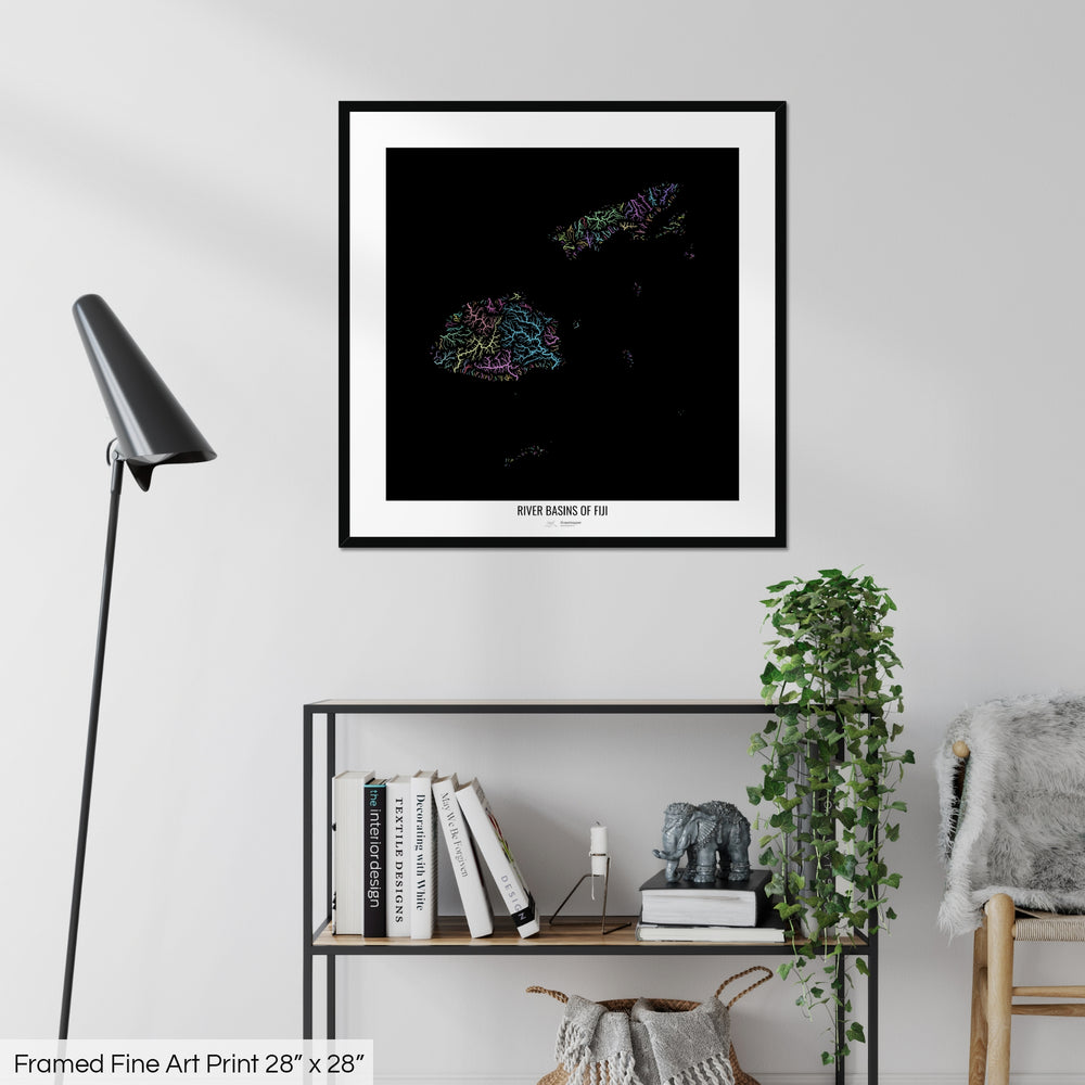 A colourful Grasshopper Geography map on a white wall, home decor in a living room. The map is in a black frame with a thick white mat. The title of the map is printed on the mat. The map hangs above a black shelf with plants and books on. A black lamp stands in the corner.