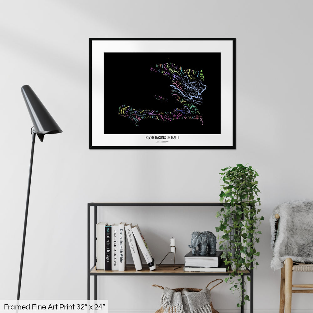 A colourful Grasshopper Geography map on a white wall, home decor in a living room. The map is in a black frame with a thick white mat. The title of the map is printed on the mat. The map hangs above a black shelf with plants and books on. A black lamp stands in the corner.