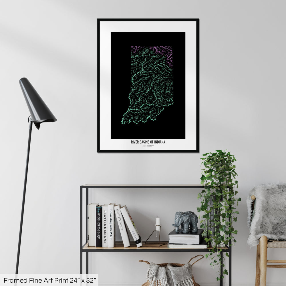 A colourful Grasshopper Geography map on a white wall, home decor in a living room. The map is in a black frame with a thick white mat. The title of the map is printed on the mat. The map hangs above a black shelf with plants and books on. A black lamp stands in the corner.
