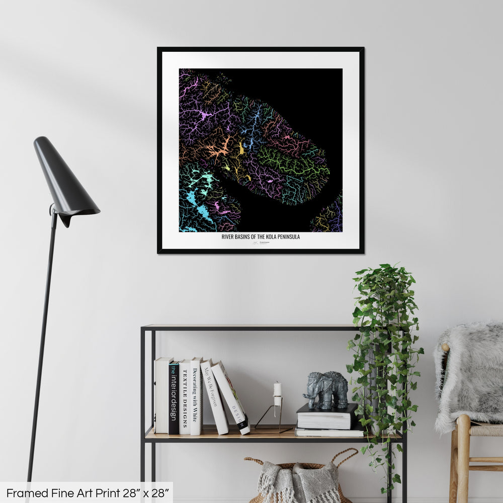 A colourful Grasshopper Geography map on a white wall, home decor in a living room. The map is in a black frame with a thick white mat. The title of the map is printed on the mat. The map hangs above a black shelf with plants and books on. A black lamp stands in the corner.