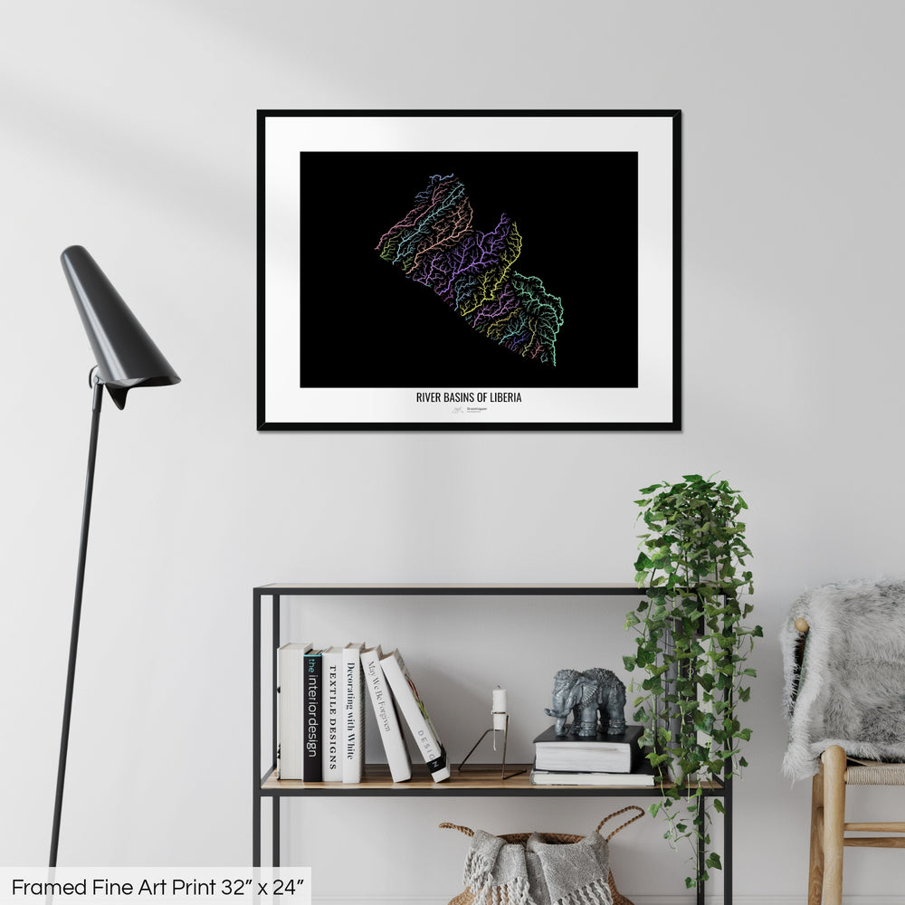 A colourful Grasshopper Geography map on a white wall, home decor in a living room. The map is in a black frame with a thick white mat. The title of the map is printed on the mat. The map hangs above a black shelf with plants and books on. A black lamp stands in the corner.