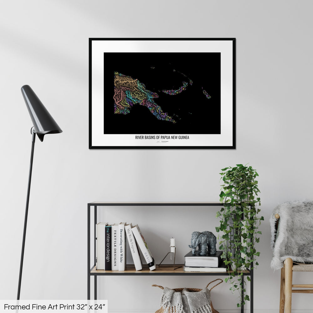 A colourful Grasshopper Geography map on a white wall, home decor in a living room. The map is in a black frame with a thick white mat. The title of the map is printed on the mat. The map hangs above a black shelf with plants and books on. A black lamp stands in the corner.