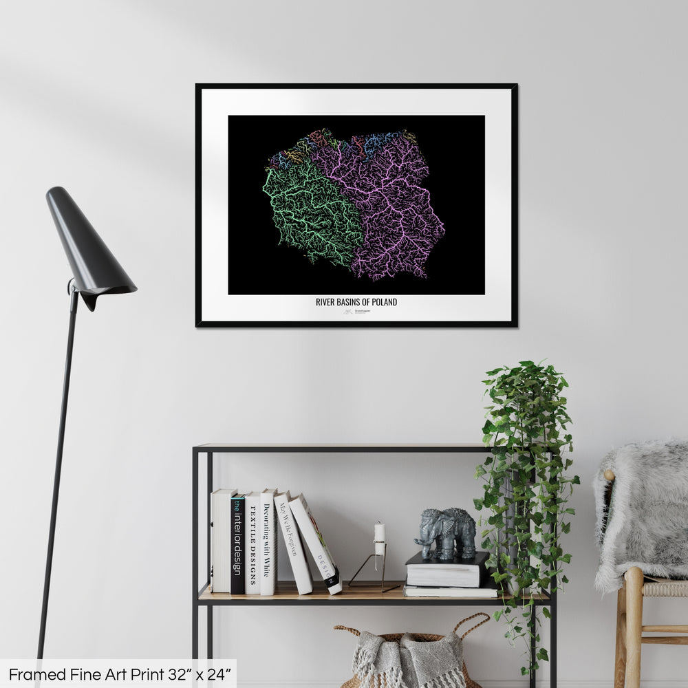 A colourful Grasshopper Geography map on a white wall, home decor in a living room. The map is in a black frame with a thick white mat. The title of the map is printed on the mat. The map hangs above a black shelf with plants and books on. A black lamp stands in the corner.