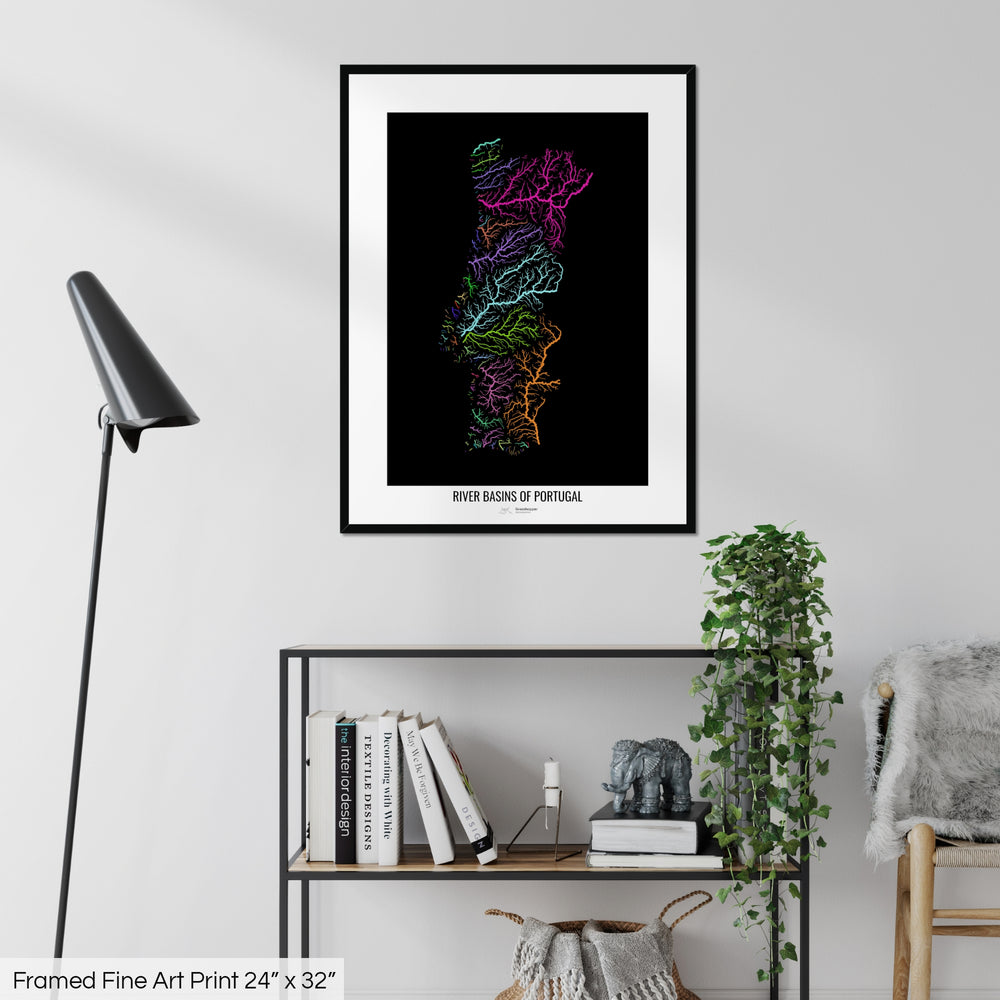 A colourful Grasshopper Geography map on a white wall, home decor in a living room. The map is in a black frame with a thick white mat. The title of the map is printed on the mat. The map hangs above a black shelf with plants and books on. A black lamp stands in the corner.