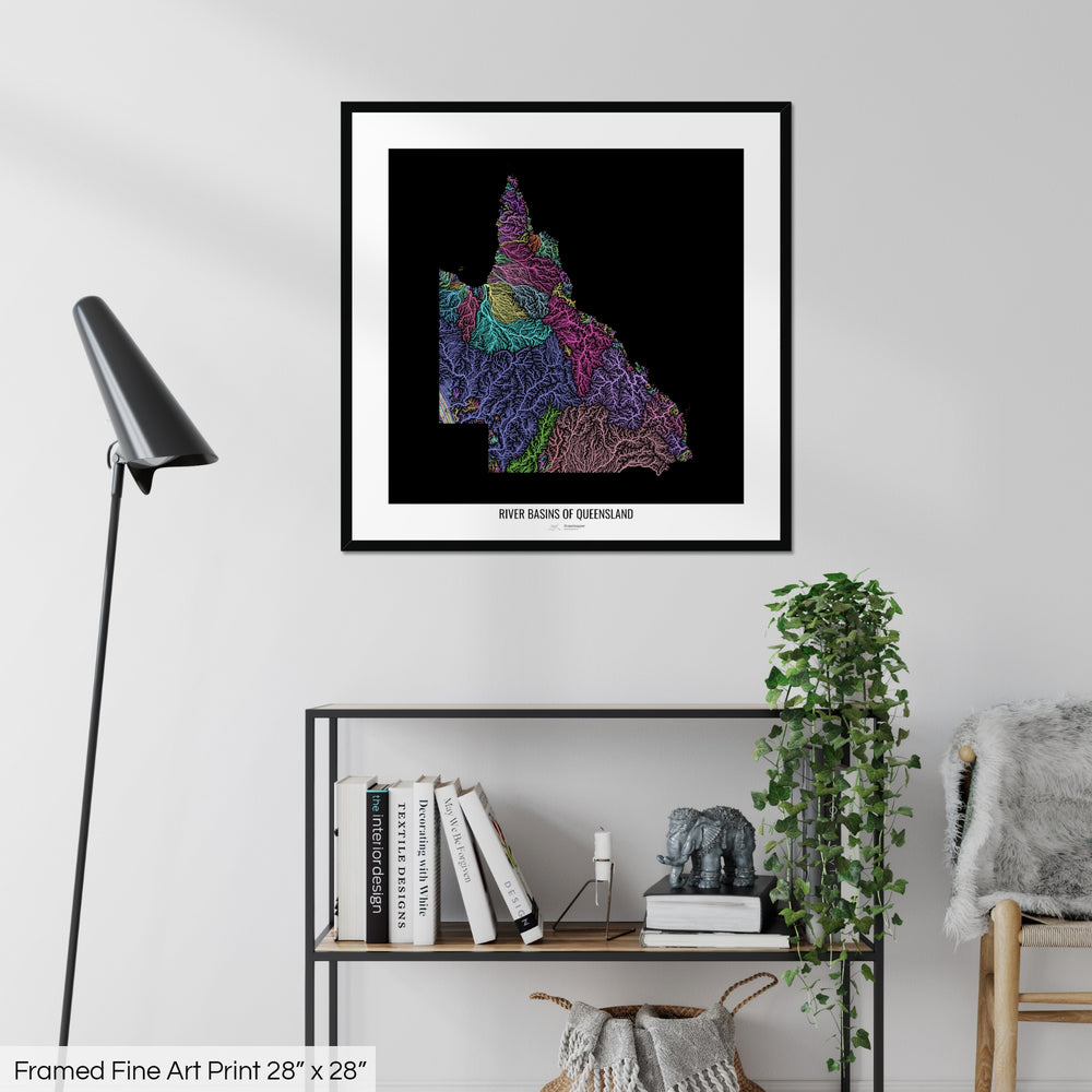 A colourful Grasshopper Geography map on a white wall, home decor in a living room. The map is in a black frame with a thick white mat. The title of the map is printed on the mat. The map hangs above a black shelf with plants and books on. A black lamp stands in the corner.